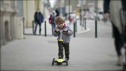 Cute little baby toddler riding scooter outside in street