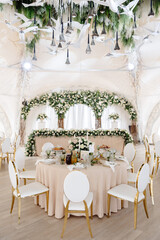 Elegant wedding reception hall featuring round tables, white and gold chairs, and floral arrangements