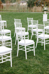 White chiavari chairs standing on lawn for wedding ceremony are waiting for guests
