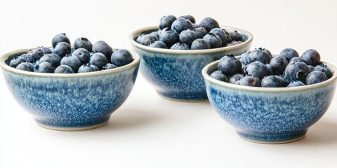 Three textured blue bowls filled with fresh blueberries arranged in a cluster on a clean white background creating a vibrant and inviting scene
