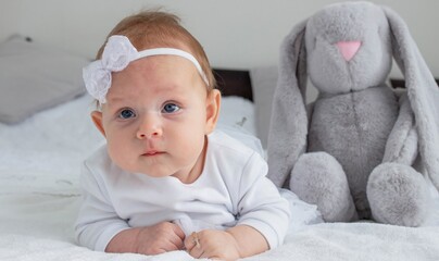 The baby is dressed in a white dress and lies with a bunny, a chain with a cross. Baptism of a child