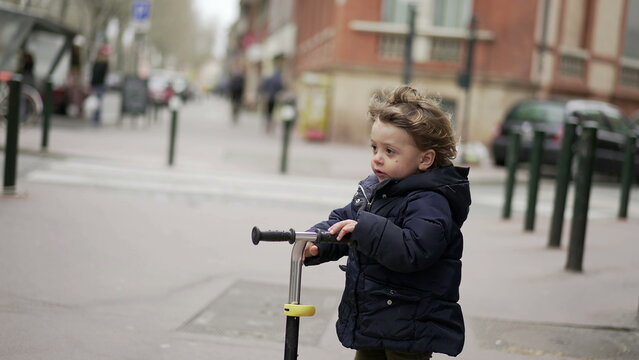 Happy little todder riding scooter in urban sidewalk street