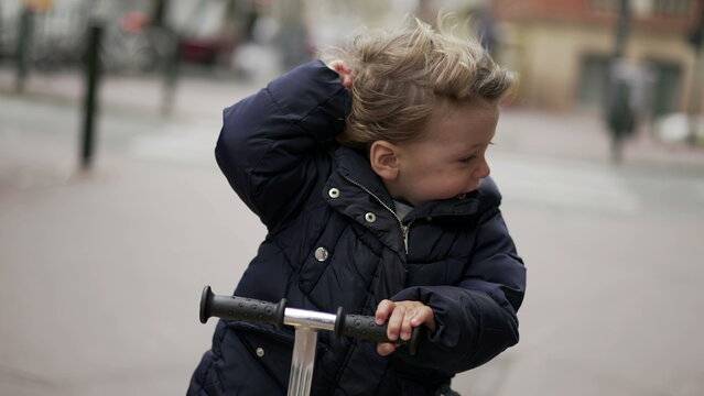 Happy little todder riding scooter in urban sidewalk street
