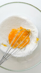 A glass bowl filled with flour and egg yolk, being whisked for baking, symbolizes preparation for Christmas baking