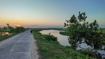 A serene rural landscape at sunset with a solitary figure on a country road, evoking tranquility...