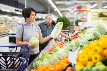 Mature female customer selects savoy cabbage with interest in grocery department of supermarket