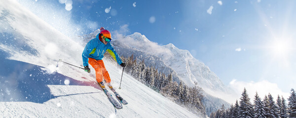 A skier skiing downhill a groomed alpine slope during sunny winter day