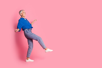 Full length photo of excited good mood woman wear blue shirt walking empty space isolated pink color background