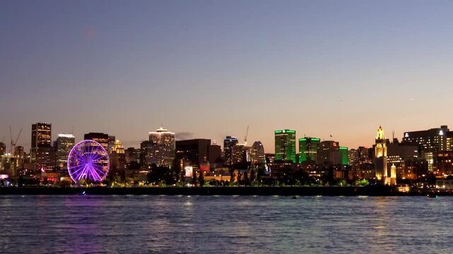 Old Port of Montreal and downtown skyline at night. Colorful buildings lights reflected in water. Montreal city, Quebec, Canada. Ferris wheel.
