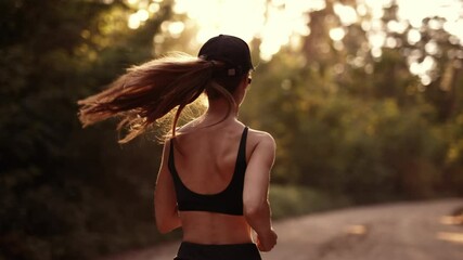 A young sporty woman runner is listening to music in earphones and training workout. Slim fitness girl is jogging outdoor. Concept of workouts running and healthy sport lifestyle