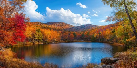 Fototapeta premium Vibrant autumn landscape with orange and red foliage reflecting in calm lake under blue sky and fluffy white clouds in serene nature setting