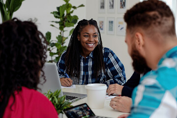 A diverse team engaged in an enthusiastic discussion around a table in a bright office. Laptops and plants create a collaborative atmosphere