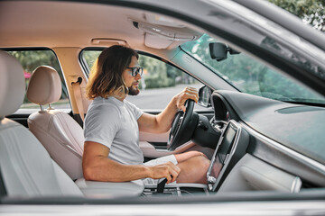 Man driving a car, focusing on the road with a relaxed expression, wearing sunglasses, in a modern vehicle interior