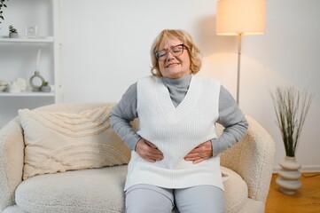 Senior woman sitting on her bed has stomach ache