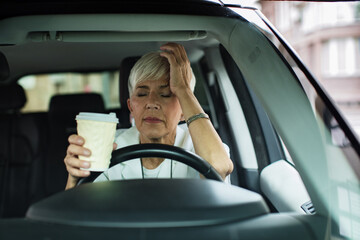 Senior female medical professional holding head in stress during coffee break in car