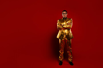 Young gentleman in shiny golden suit poses confidently against a striking red background, exuding...