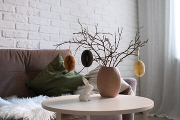 A beautifully cozy living room with modern easter home decor that includes vase with dry branches and eggs, ceramic rabbit, on coffee table.