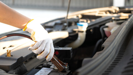 Action of a technician hand is using an emergency clamping kit to clamp on positive polar for jumping the 12V car battery. Transportation troubleshooting and reparing scene, close-up.