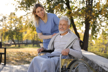 Caregiver assisting senior man on wheelchair in park. Home health care service