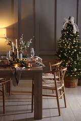 Christmas table setting with stylish dishware, glasses and burning candles in festive decorated room