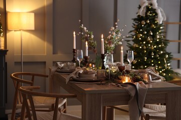 Christmas table setting with stylish dishware, glasses and burning candles in festive decorated room