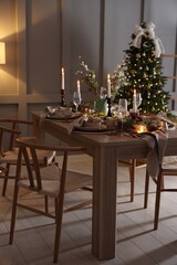 Christmas table setting with stylish dishware, glasses and burning candles in festive decorated room