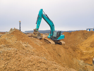 Heavy machinery excavates earth at a construction site under a cloudy sky in the early morning hours