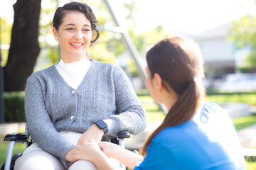 Young caucasian nurse comforting with patient while sitting on wheelchair in outdoor park, doctor...