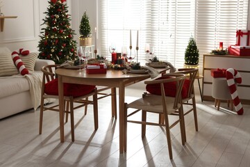 Christmas table setting with stylish dishware, glasses and burning candles in festive decorated room