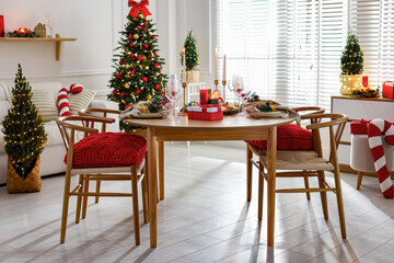 Christmas table setting with stylish dishware, glasses and burning candles in festive decorated room