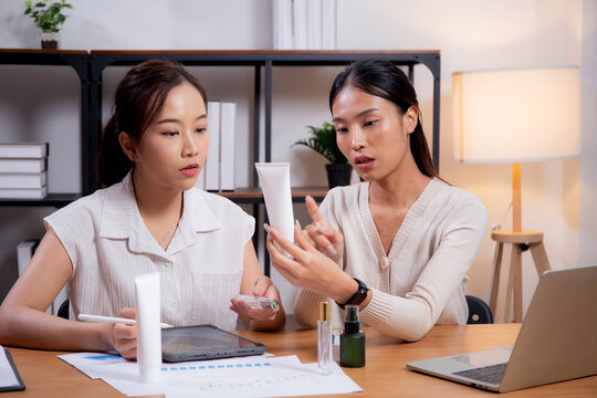 Two asian businesswoman testing and researching cosmetic product or cream in bottle in office, two business woman creative with planning project design package of skincare, development and business.