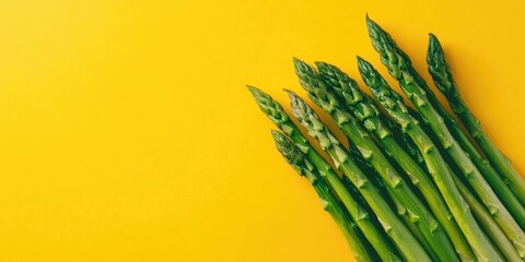 Fresh green asparagus neatly arranged in a row on a vibrant yellow backdrop with ample negative space on the left for text placement.