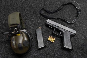 A pistol with a magazine and cartridges, active headphones and protective glasses on a table in a...