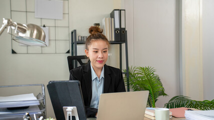 Businesswoman sitting at desk on couch in workplace or at home working on laptop and analyzing data on charts and graphs and writing on papers to make business plan and strategies for company.