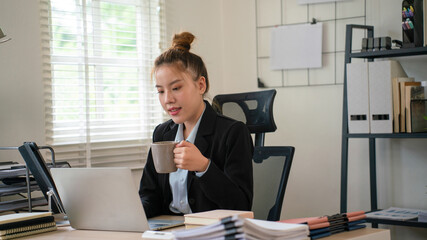 Fototapeta premium Businesswoman sitting at desk on couch in workplace or at home working on laptop and analyzing data on charts and graphs and writing on papers to make business plan and strategies for company.