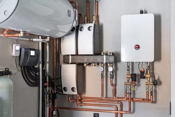 Heating system equipment in a boiler room of modern private house. Wall installation of electric boiler device, valves, pumps, cooper tubing, water heater, automatic controller in a single family home © GarkushaArt