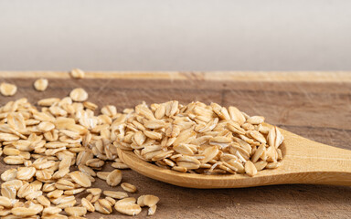 Rustic wooden spoon filled with rolled oats, surrounded by scattered oats on a wooden surface,...