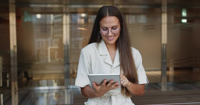 Attractive European businesslady working on tablet device in workspace, organizing upcoming meetings or schedules, reviewing performance metrics, designing presentation, drafting or editing contracts