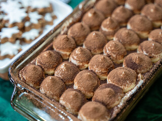 Glass dish of tiramisu topped with cocoa powder, alongside iced cookies
