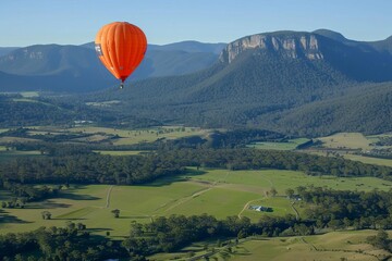 Obraz premium A vibrant hot air balloon floats over lush green landscapes and mountains under a clear blue sky.