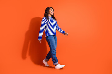Full length photo of shiny attractive lady dressed striped shirt walking empty space isolated orange color background