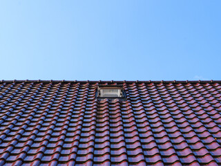 Ziegeldach mit kleinem Fenster unter blauem Himmel, minimalistische Perspektive