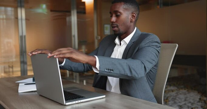 African businessman successfully accomplishes his work on laptop at workplace table, completing online task, closes device, leans back in chair, exuding sense of satisfaction after productive workday