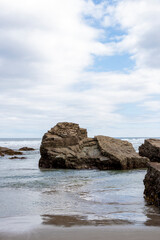 Layered rock formations surrounded by shallow ocean waters under a partly cloudy sky, creating a serene coastal scene.