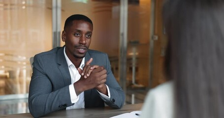African businessman shaking hands female colleague seated at desk in boardroom, parties establishing partnership, expressing gratitude, acknowledging mutual effort or contributions during discussion