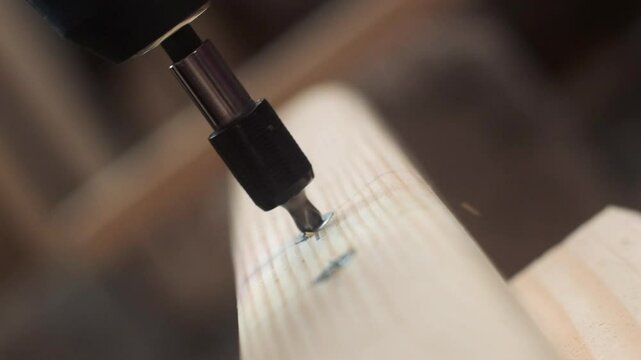 Close-up of a screw being driven into a wooden plank by an electric screwdriver. The focus is on the screw and the tip of the screwdriver, capturing the precise moment of fastening. The wood grain and
