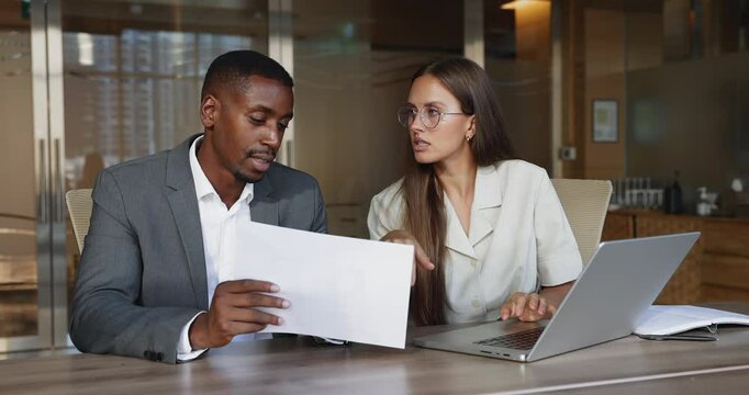 African manager explains specific points or terms and conditions from legal document to woman, reviewing contract details, ensuring client understands all relevant data before signing paper agreement