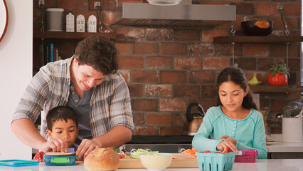 Father And Children Making Sandwiches For School Packed Lunch In Kitchen