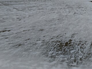 An aerial view of a frozen winter landscape showcasing an expansive sheet of ice covered with snow streaks and patches. The surface reveals intricate patterns created by wind and temperature variation