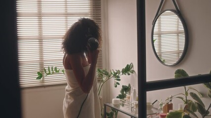 Side shot of unidentified young lady wrapped in towel drying curly hair after shower in bathroom with biophilic design, getting ready for work, morning beauty routine